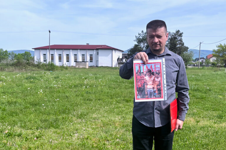 Edin Ramulić segura uma capa impressa da revista Time com uma fotografia de Fikret Alic no local do antigo campo de concentração de “Trnopolje”.